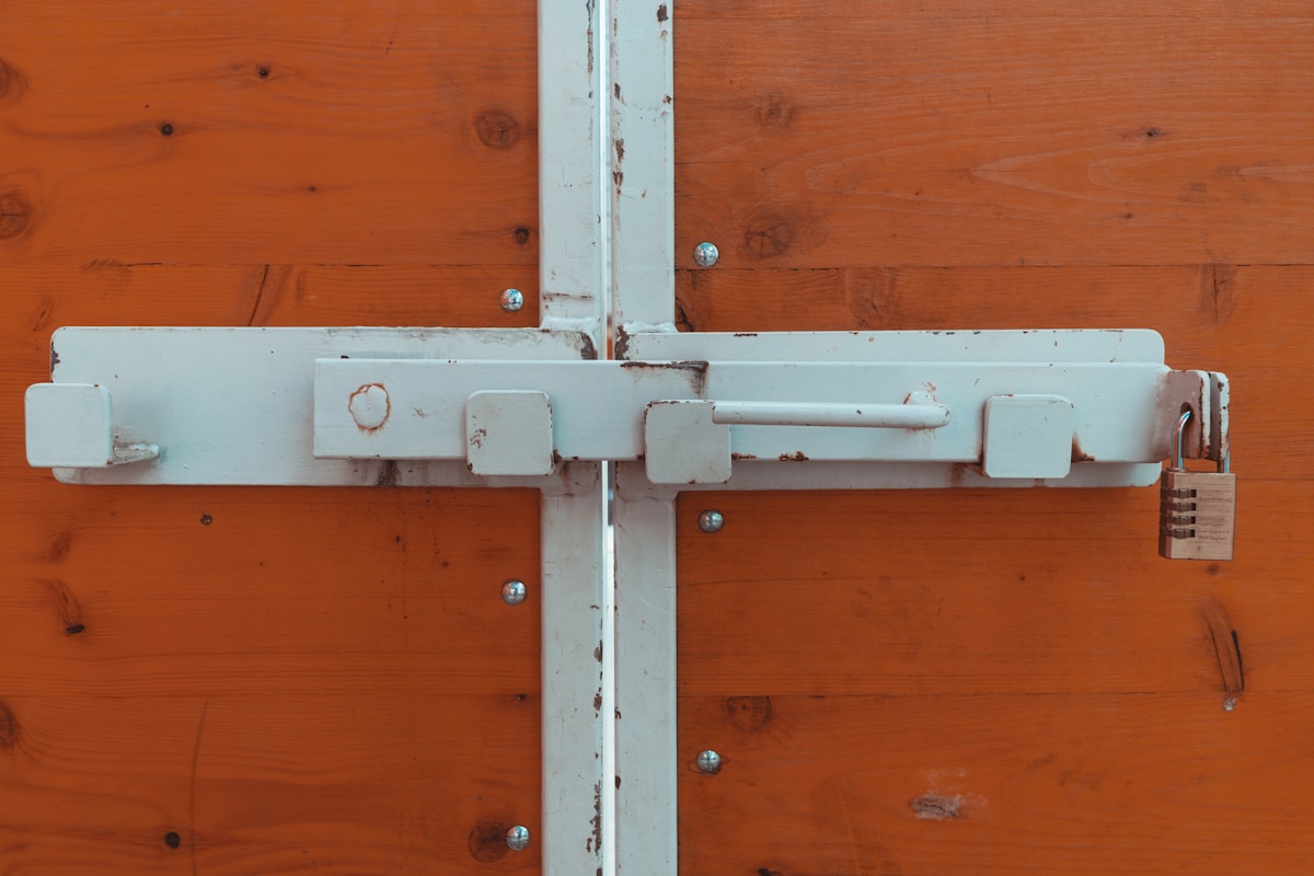Verrou de porte en métal blanc sur un fond de bois orange.
