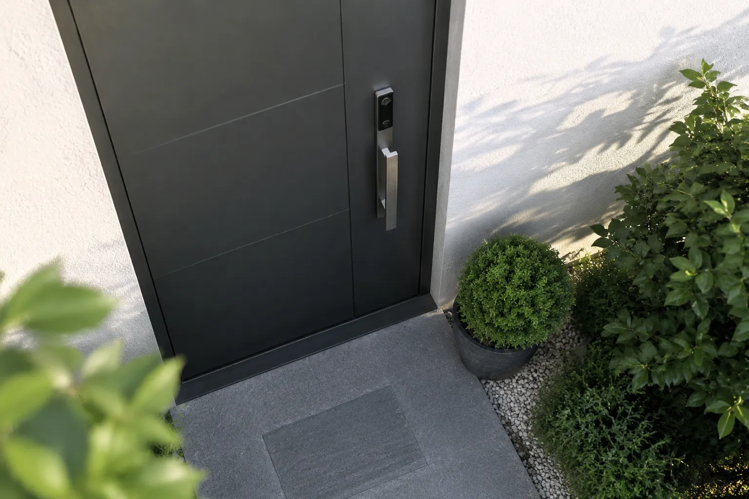 Porte d'entrée noire moderne avec plantes vertes et gravier.