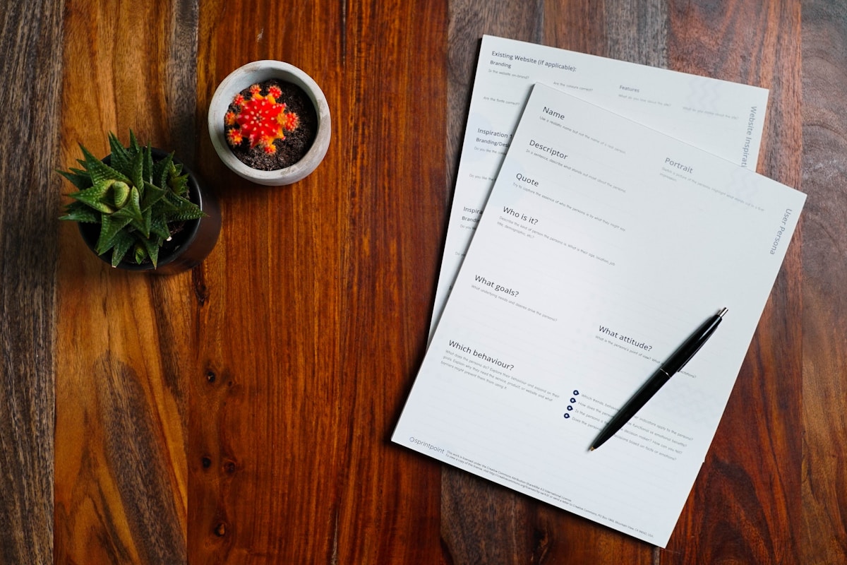 Formulaire de renseignements personnels sur un bureau en bois avec une plante et un cactus.