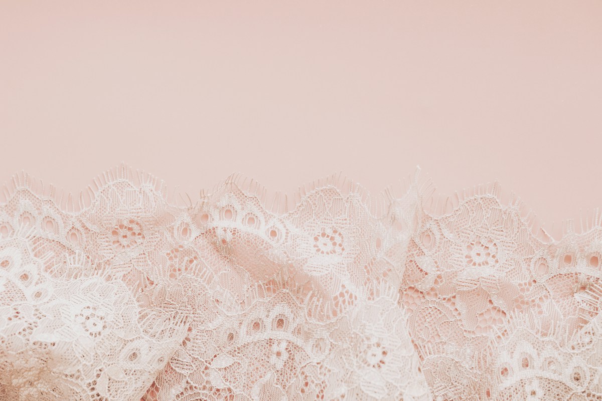 Delicate white lace fabric on a pale pink background