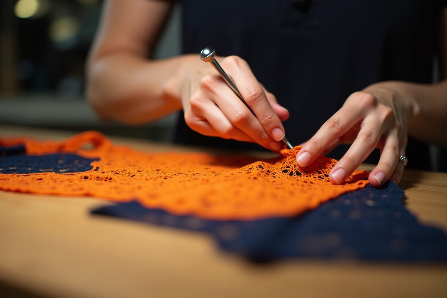 Hands working on intricate orange lace textile on dark background.