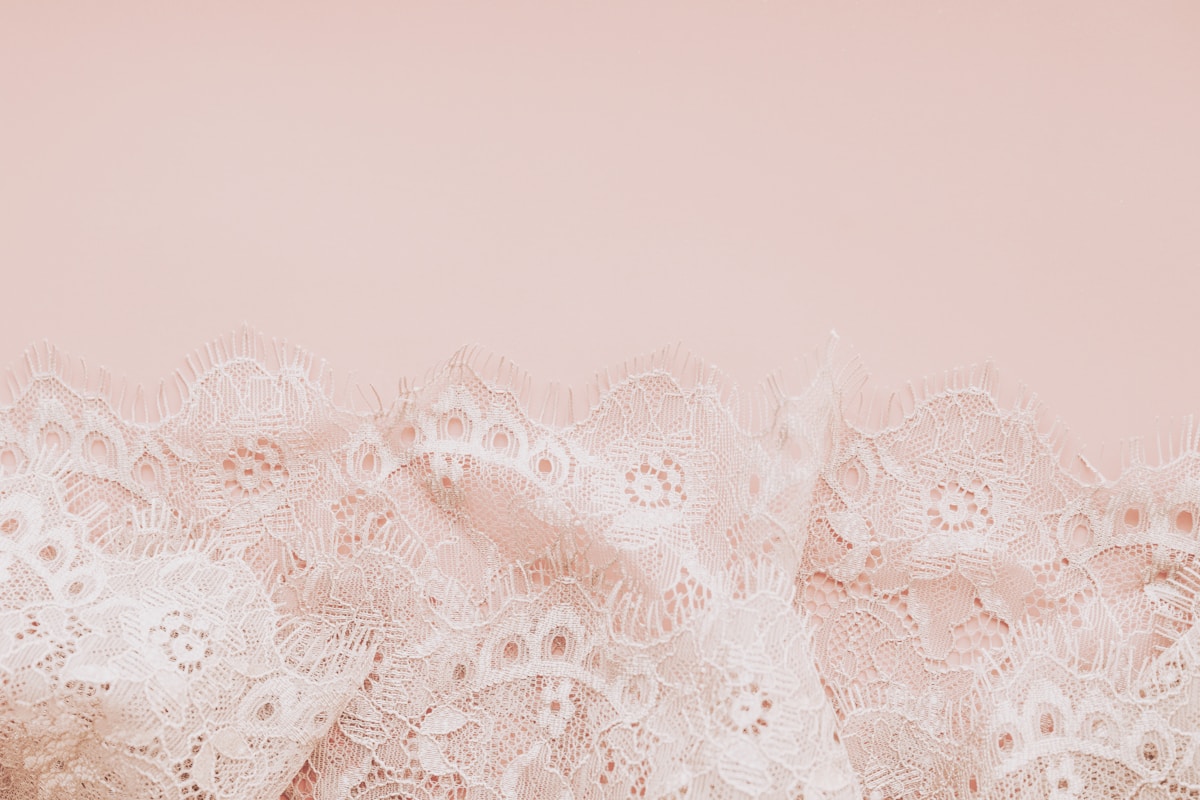 Delicate white lace fabric on a pale pink background
