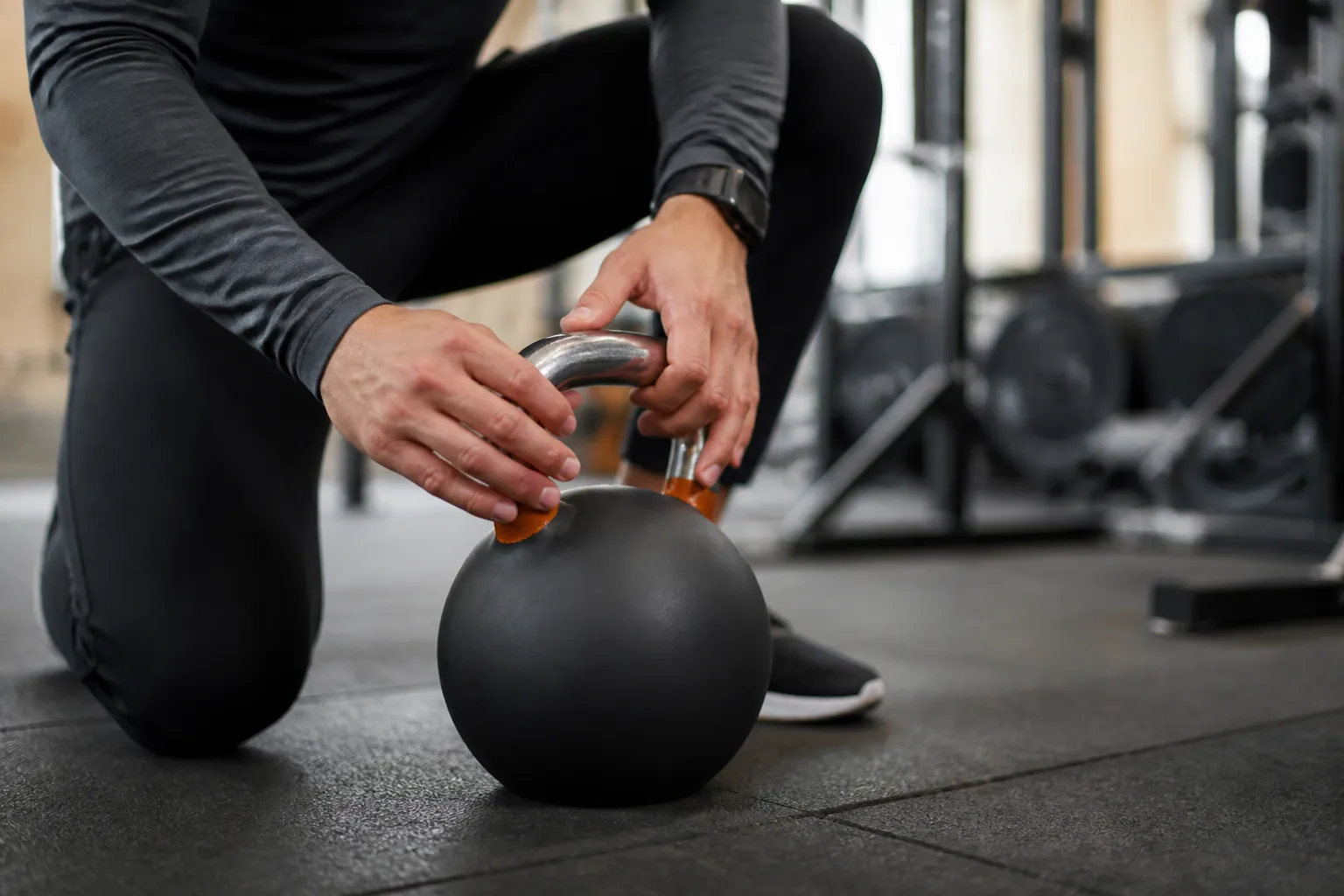 Homme en tenue de sport manipulant un haltère noir dans une salle de gym.
