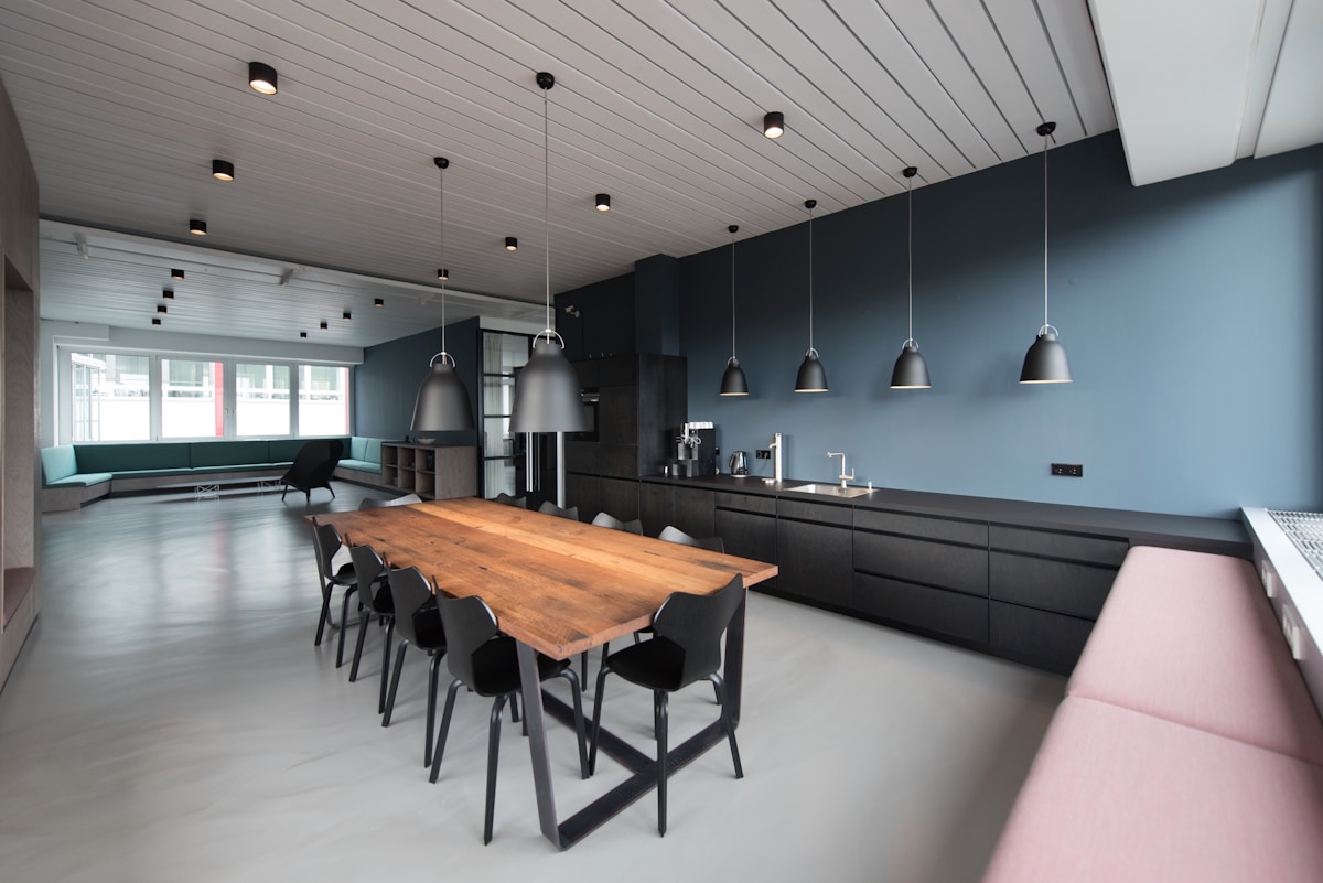 Moderne, offene Küche mit Holztisch, schwarzen Möbeln und Pendelleuchten.