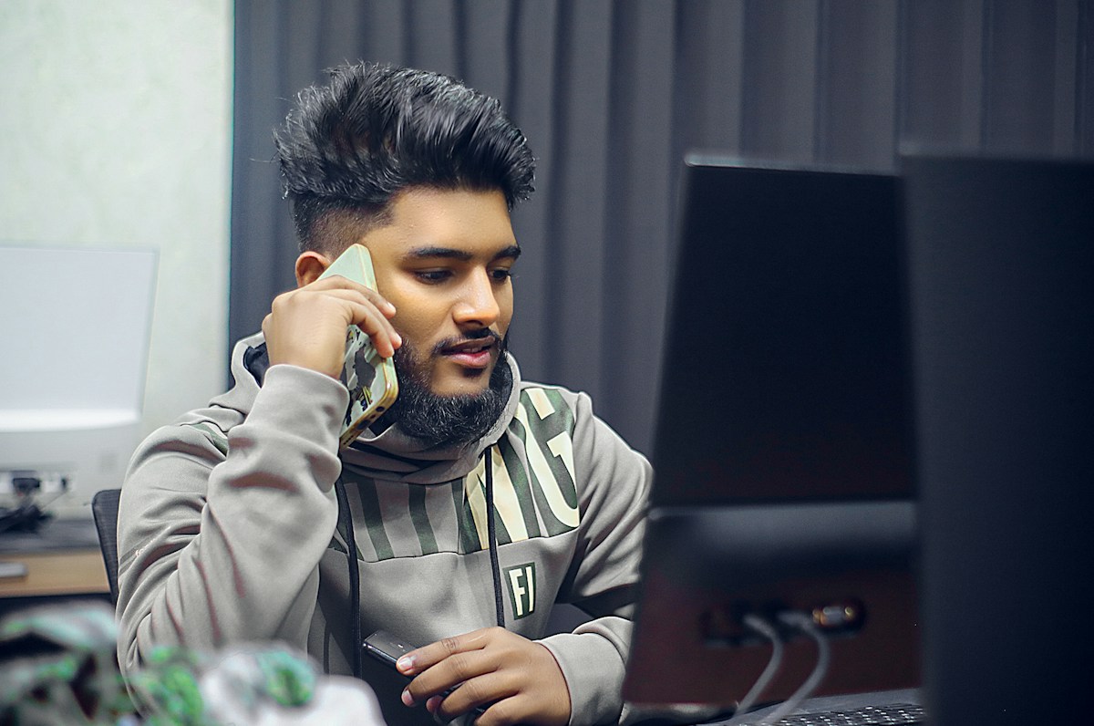 Homme barbu au téléphone devant un ordinateur de bureau.