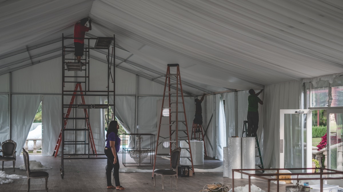 Intérieur d'un chapiteau avec échelles, chaises et préparatifs en cours.