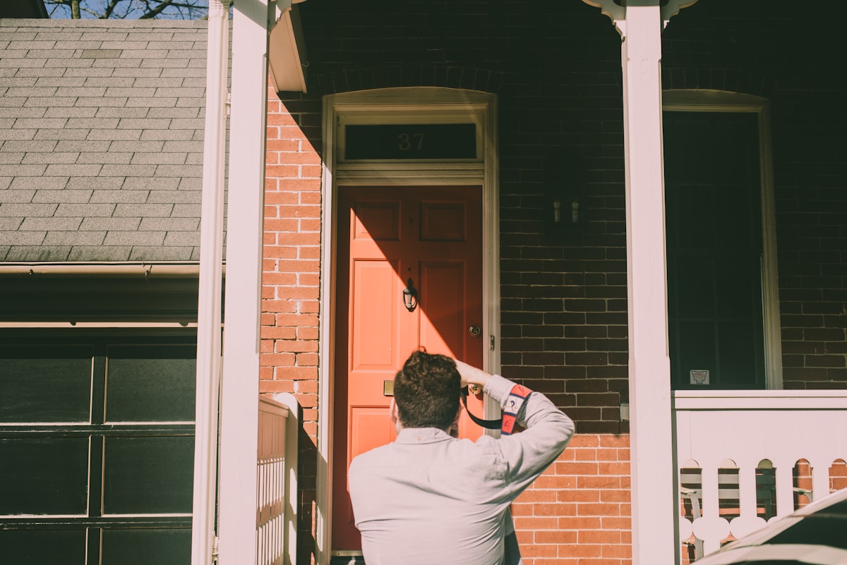 Homme ouvrant la porte d'entrée d'une maison en briques.