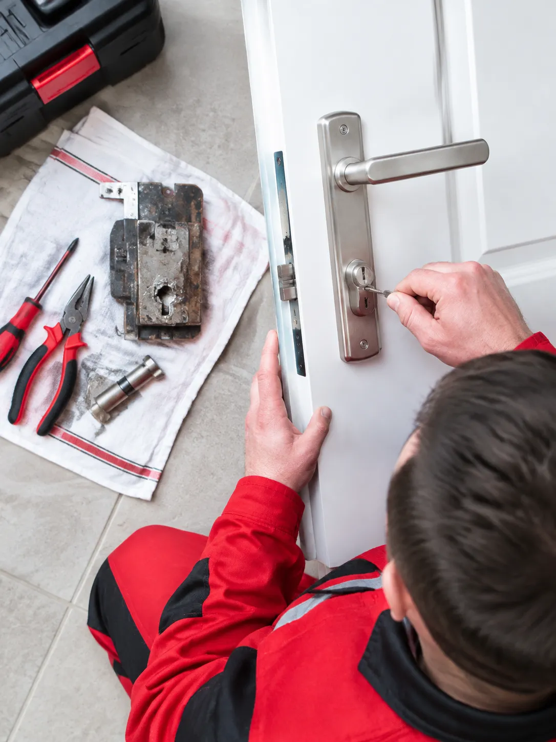 Serrurier répare une serrure de porte blanche avec outils.