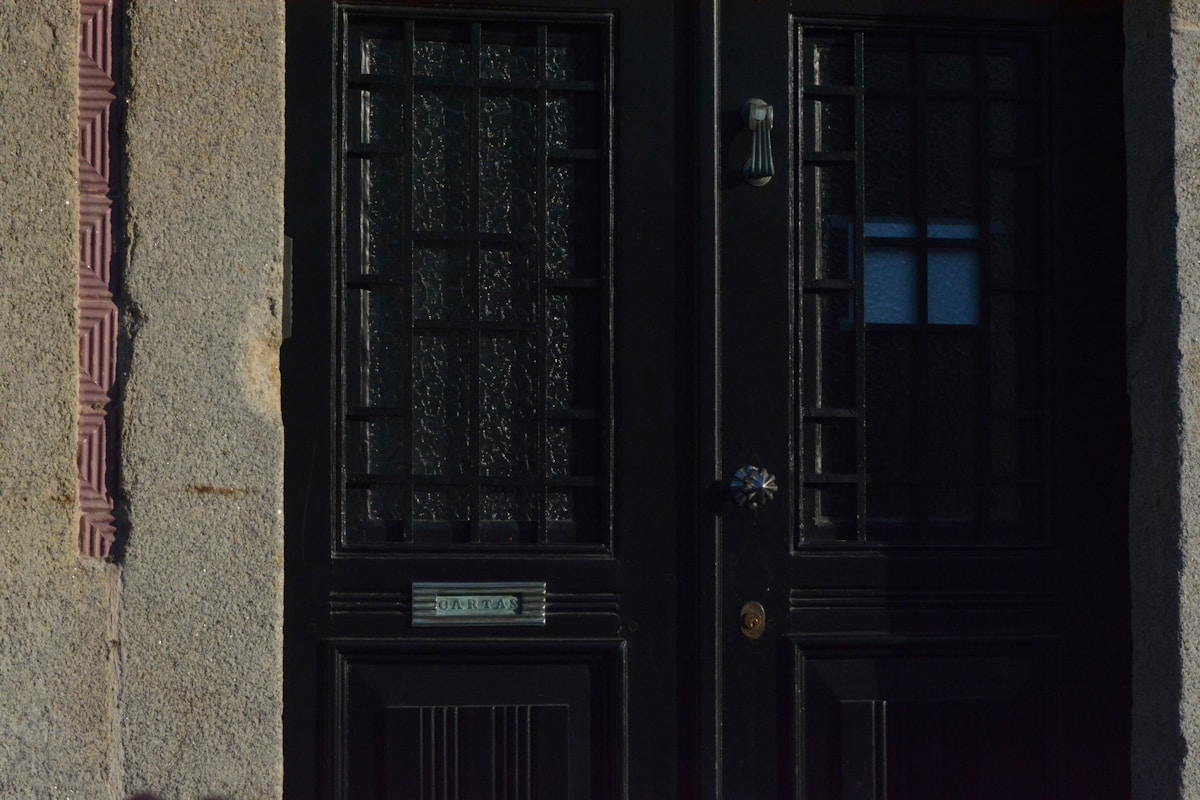 Porte d'entrée sombre avec fenêtre ornementée et plaque "Tartas".