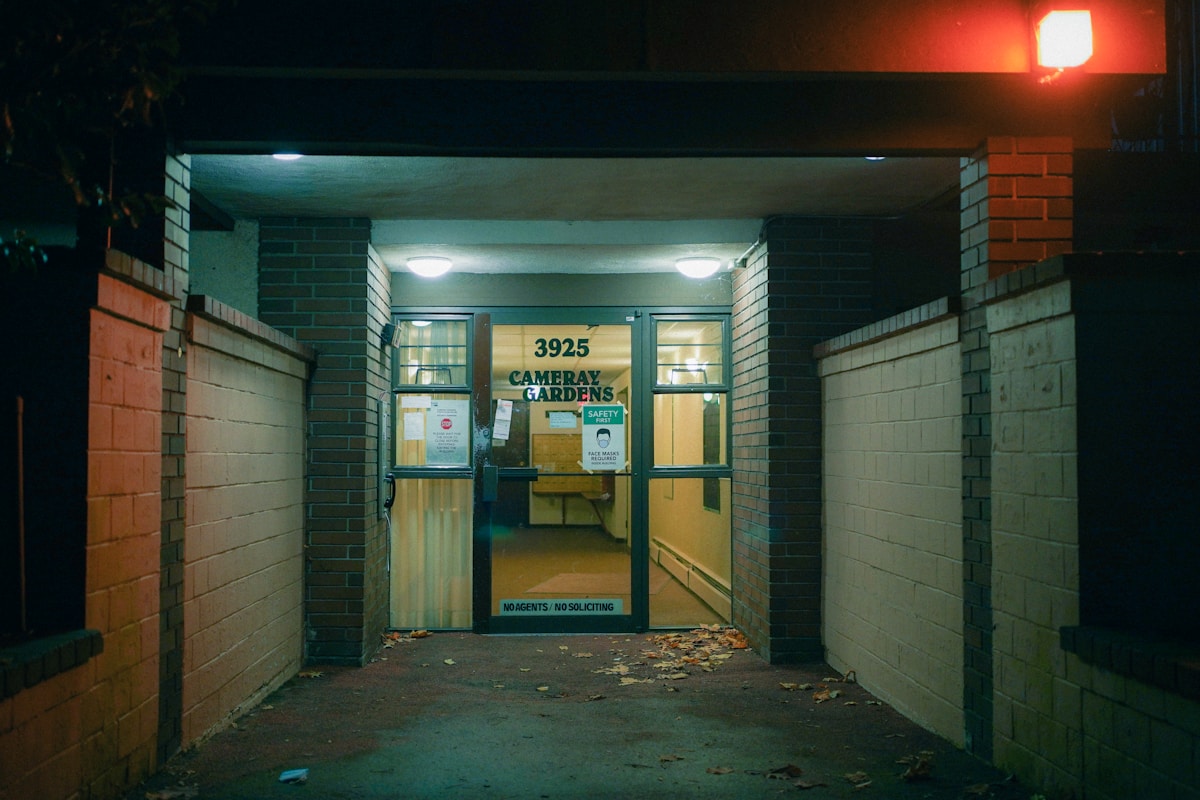 Entrée sombre d'un bâtiment résidentiel la nuit, avec un panneau indiquant "Cameray Gardens".