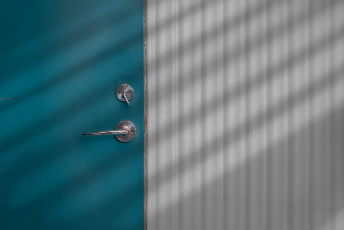 Porte en bois bleu turquoise avec poignée métallique, fond flou gris.