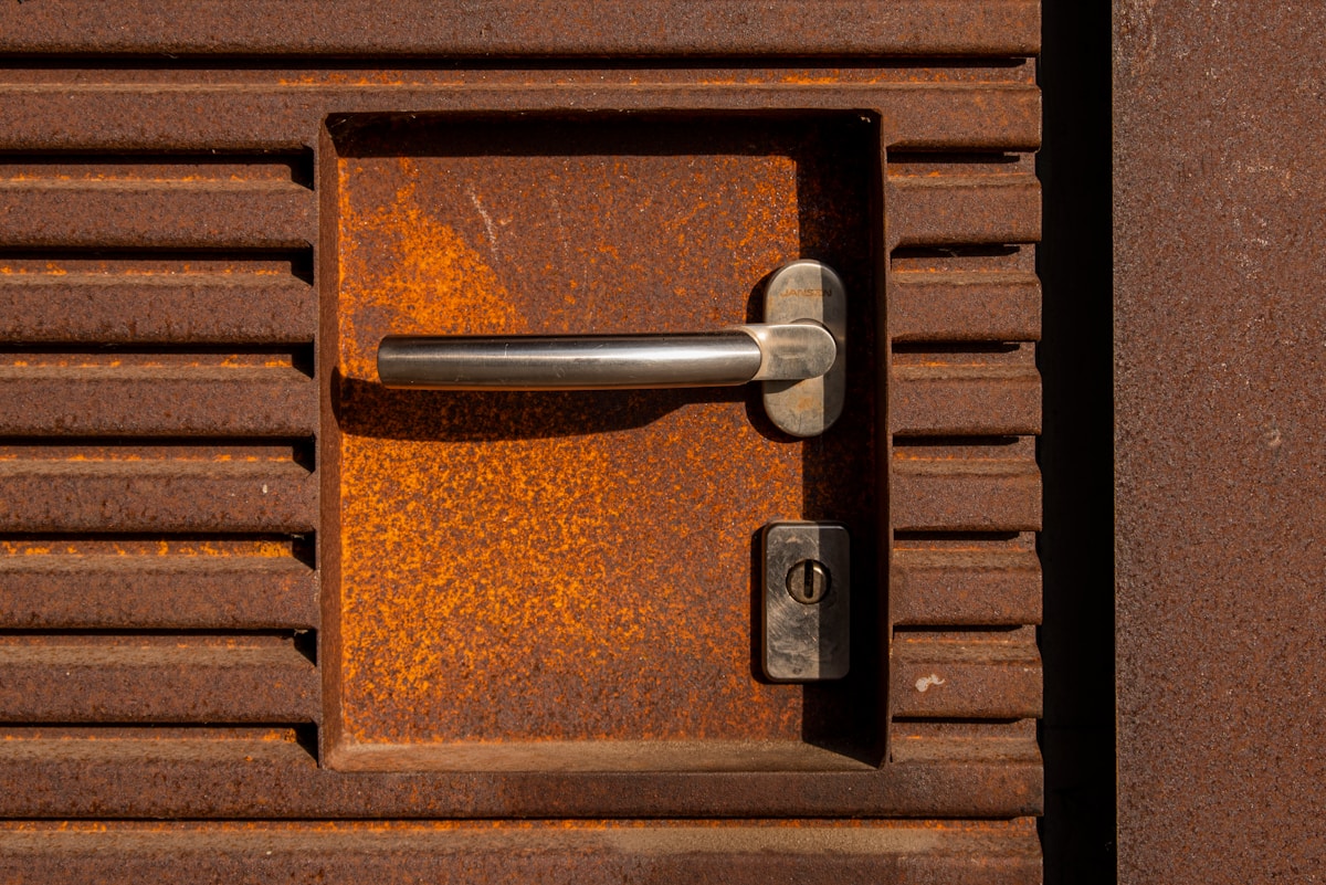 Porte en métal rouillée avec poignée et serrure.