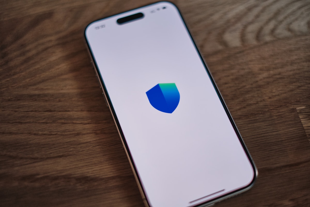 Smartphone avec l'icône d'un bouclier bleu sur un écran blanc.
