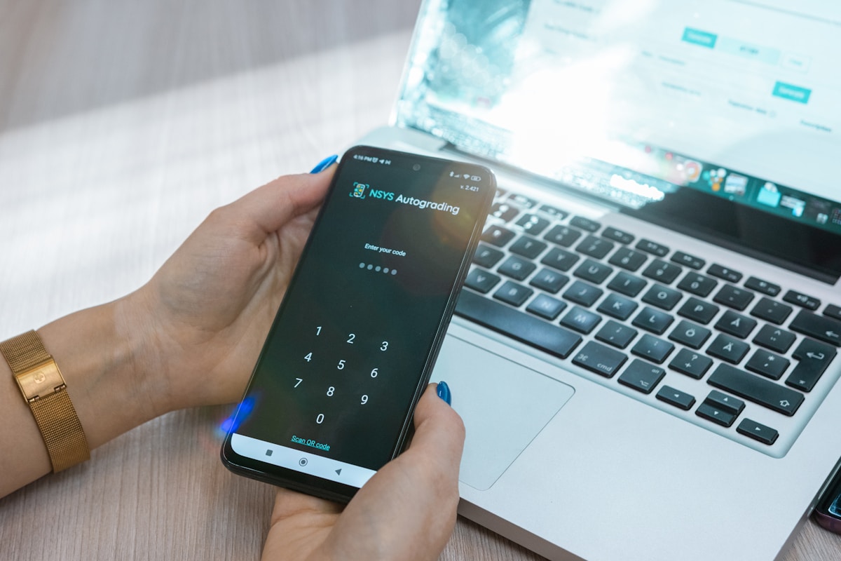 Smartphone affichant une application de négociation boursière sur un bureau avec un ordinateur portable.