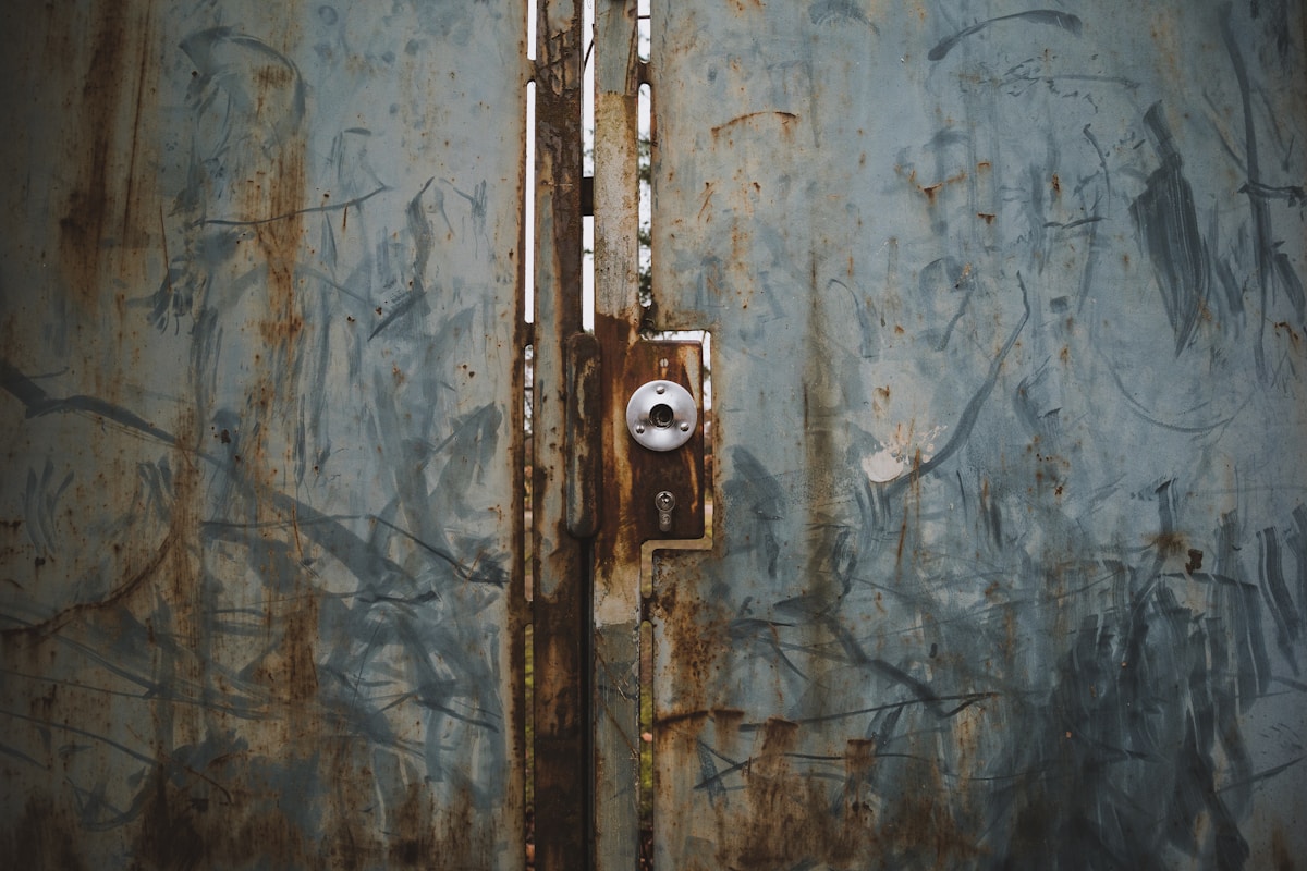 Porte en bois délabrée avec serrure rouillée sur un mur peint.