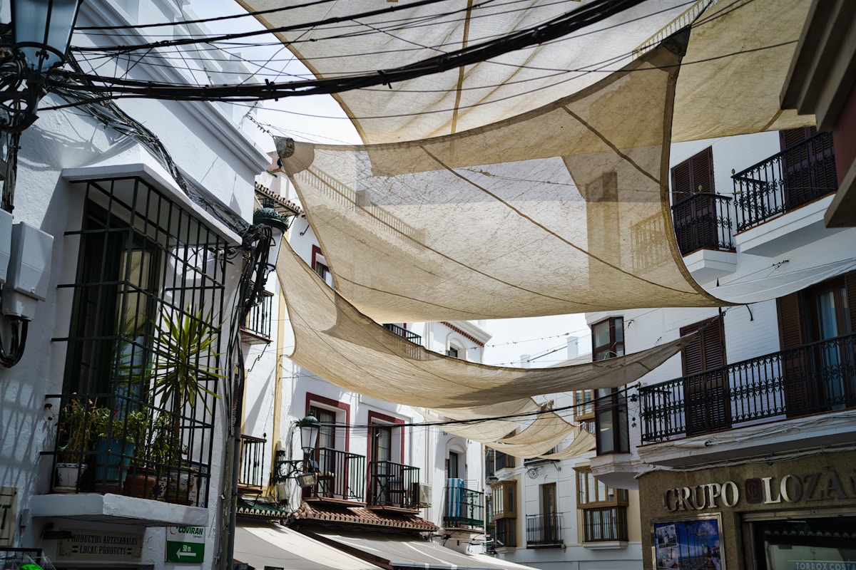 Rues étroites avec des bâtiments blancs, balcons et voiles suspendus.