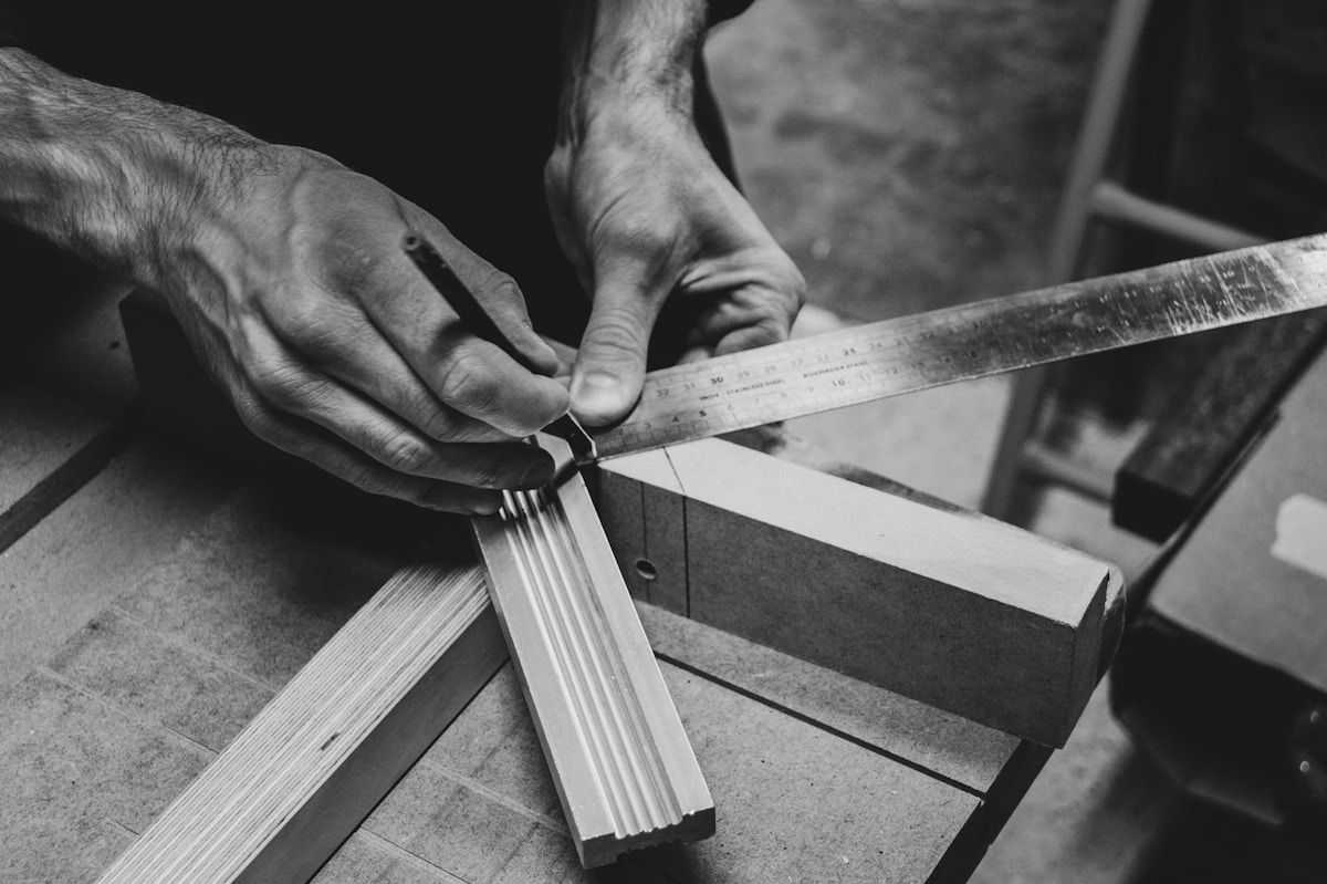 Mains d'un artisan mesurant et coupant du bois.
