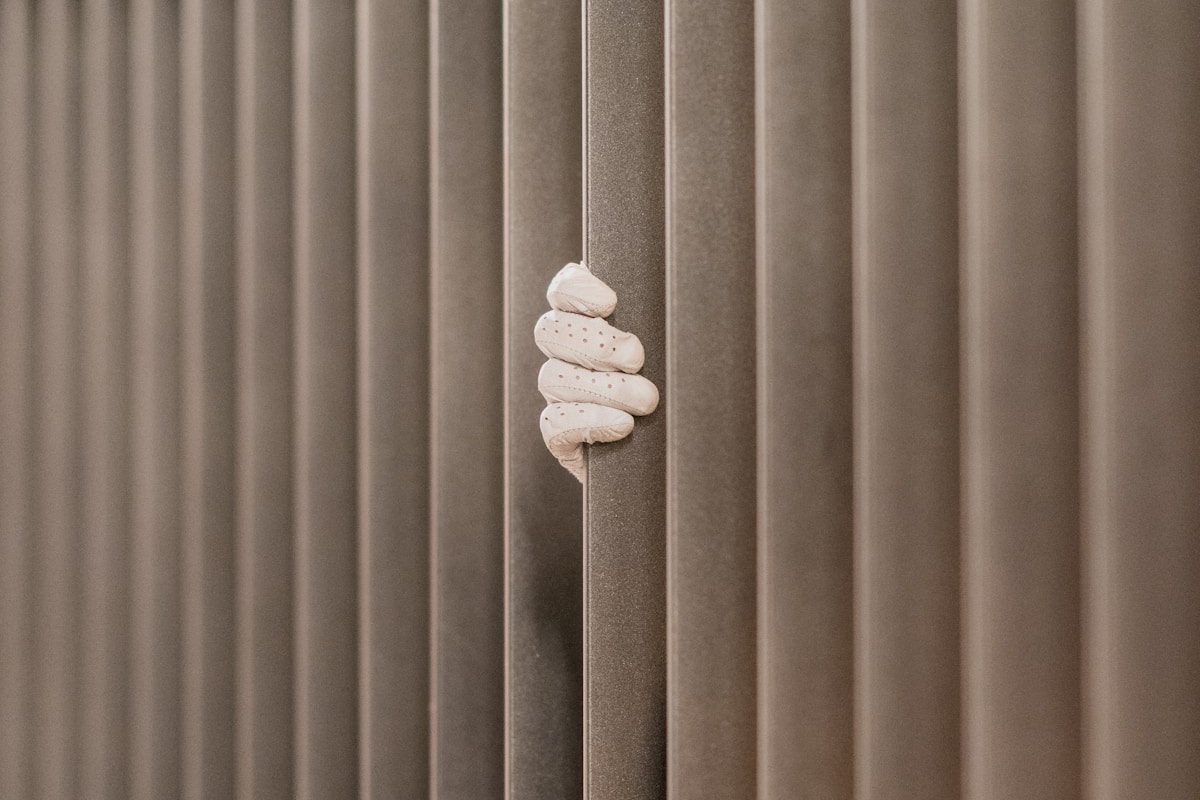 Une main gantée de blanc saisit discrètement une fente entre des panneaux verticaux.