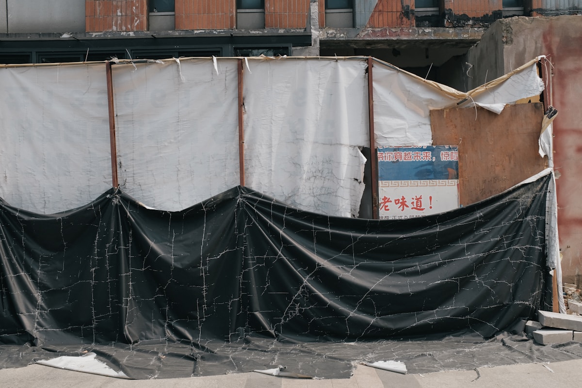 Mur de briques délabrées, barricade de bâches noires et blanches, panneau publicitaire en chinois.