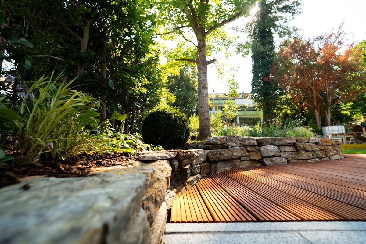 Jardin verdoyant avec sentier en bois et mur de pierre.