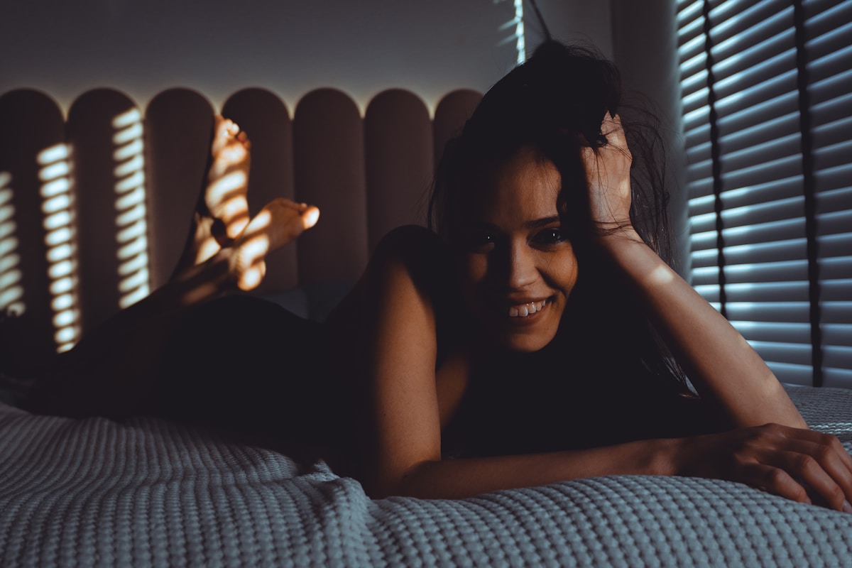 Femme souriante, cheveux noirs, lumière tamisée, fenêtre à stores.