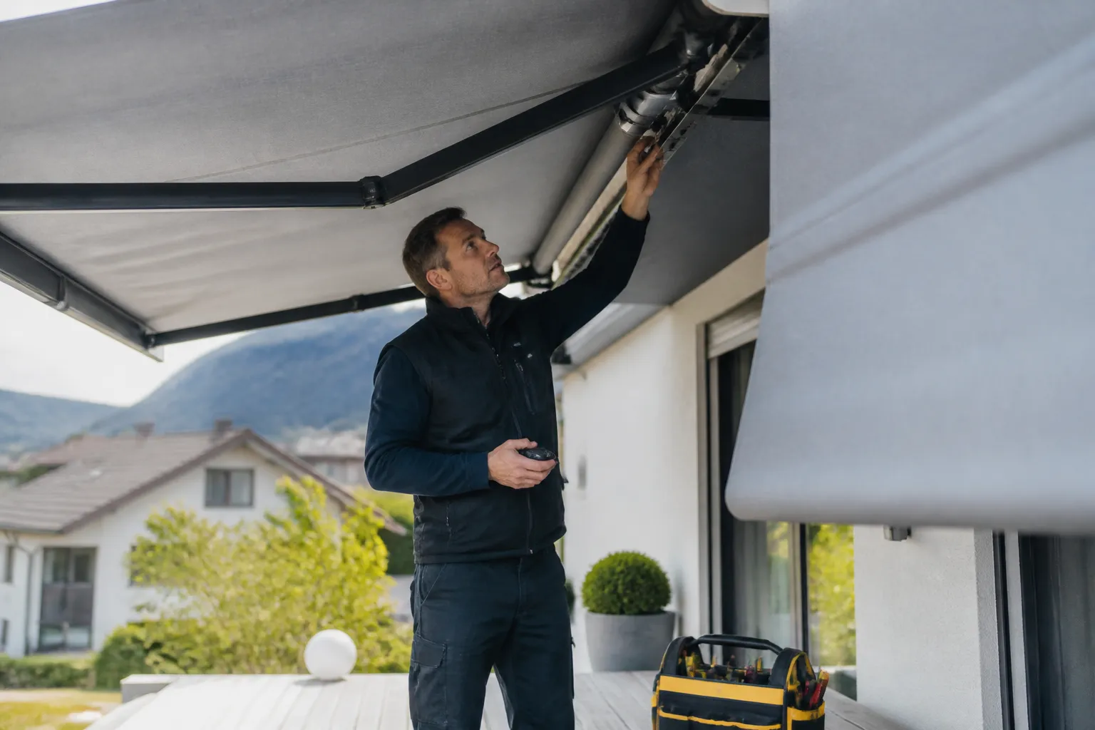 Homme installant un store extérieur sur une maison.