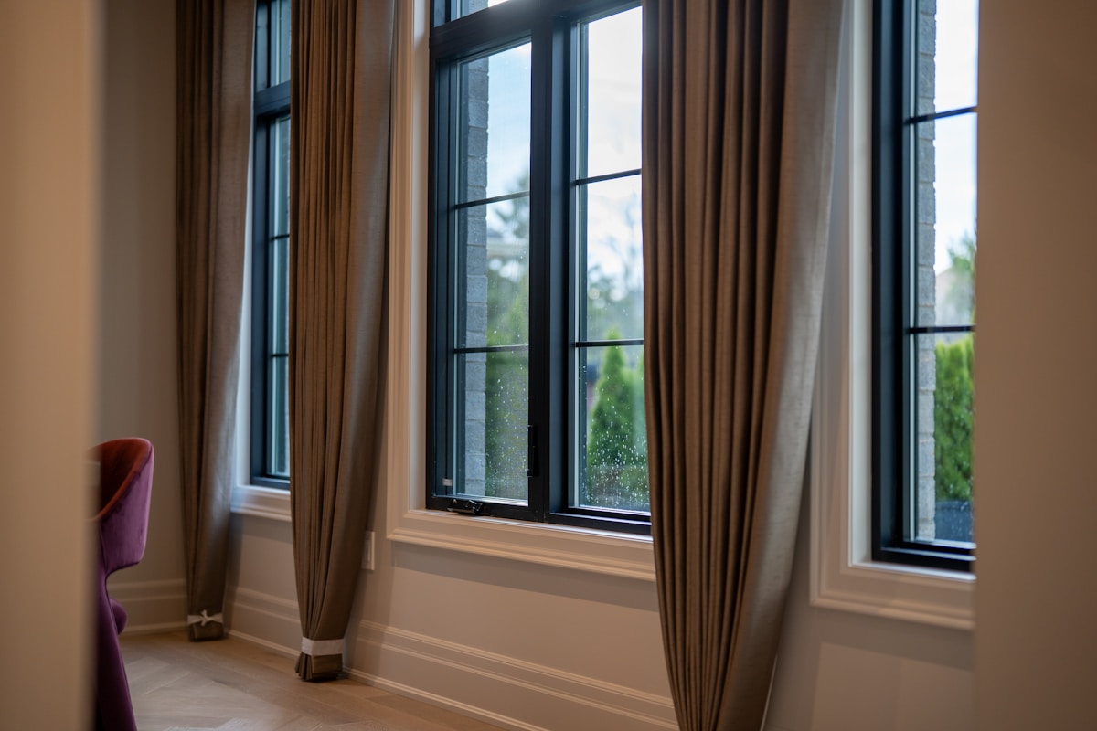 Fenêtres avec rideaux bruns, vue sur l'extérieur, gouttes de pluie sur le verre.