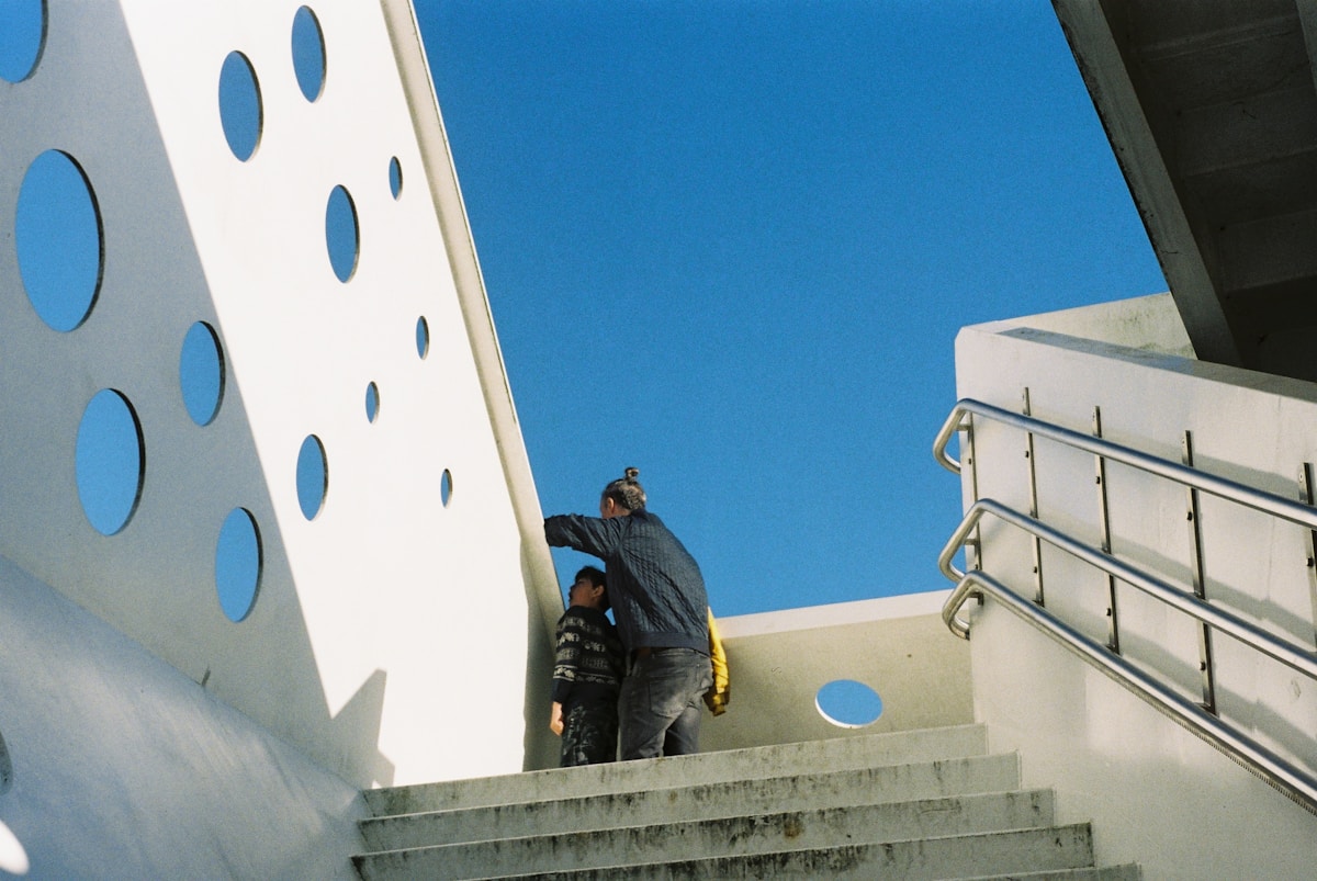Deux personnes grimpant des escaliers devant un mur blanc avec des cercles bleus.