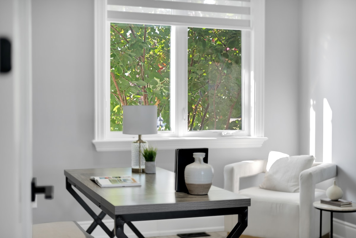 Fenêtre donnant sur un paysage verdoyant, table de travail moderne, décoration minimaliste.