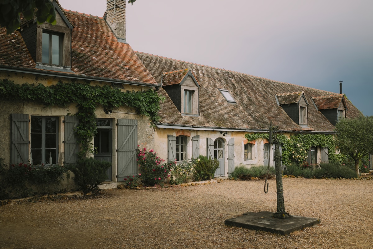 Maison de campagne rustique avec toit en tuiles, volets et plantes grimpantes.