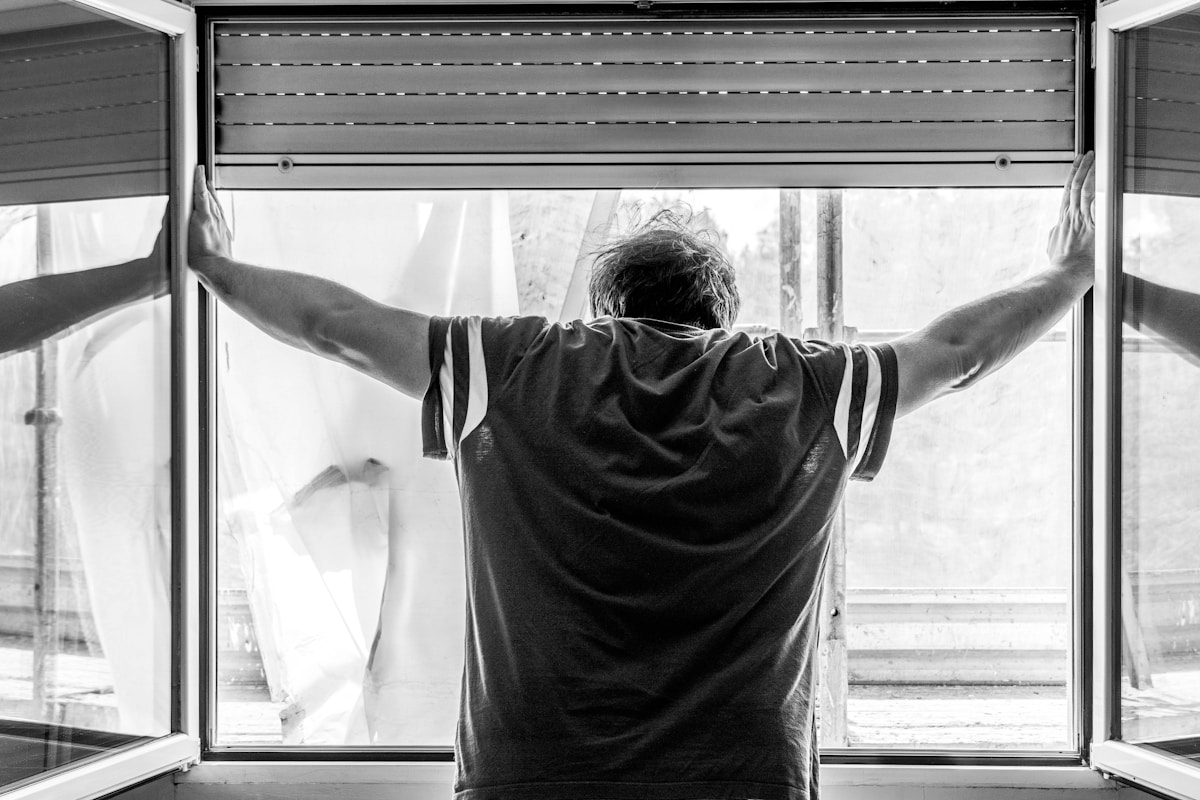 Homme ouvrant les rideaux de la fenêtre, vue arrière en noir et blanc.