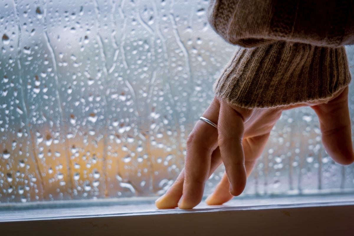 Une main sur un rebord de fenêtre avec des gouttes de pluie.
