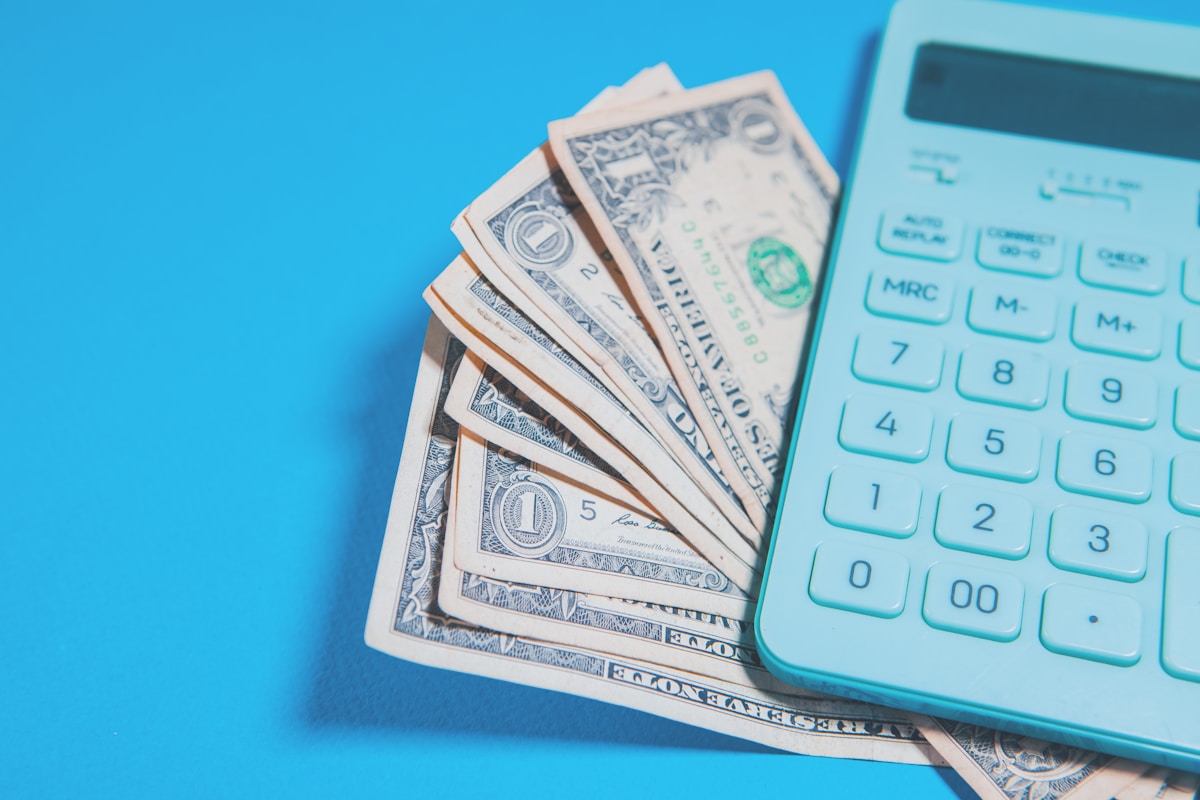 Des billets de dollars américains et une calculatrice sur fond bleu.