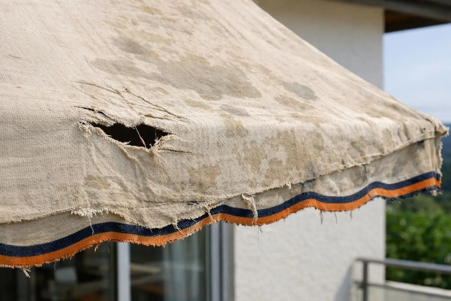 Close-up of a deteriorating beige awning fabric on a Swiss terrace showing visible tears, faded colors, water stains and worn edges, with intact house wall in background, natural daylight, real photo style