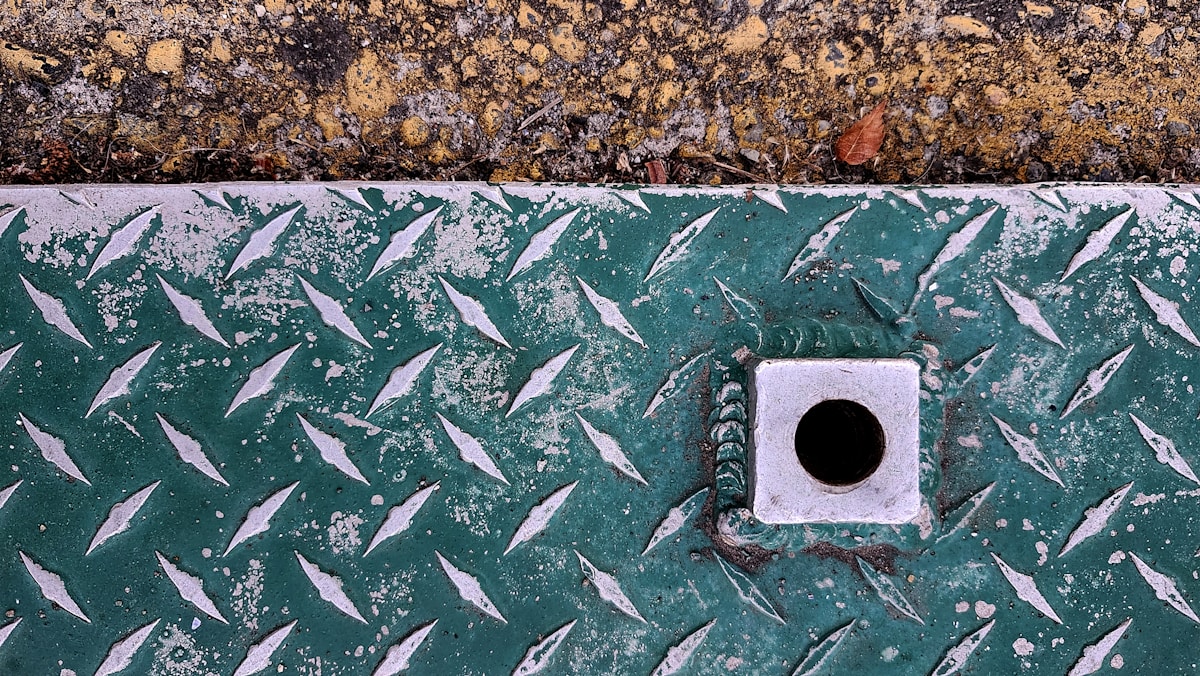 Métal à motif de diamant à côté d'un ciment texturé.