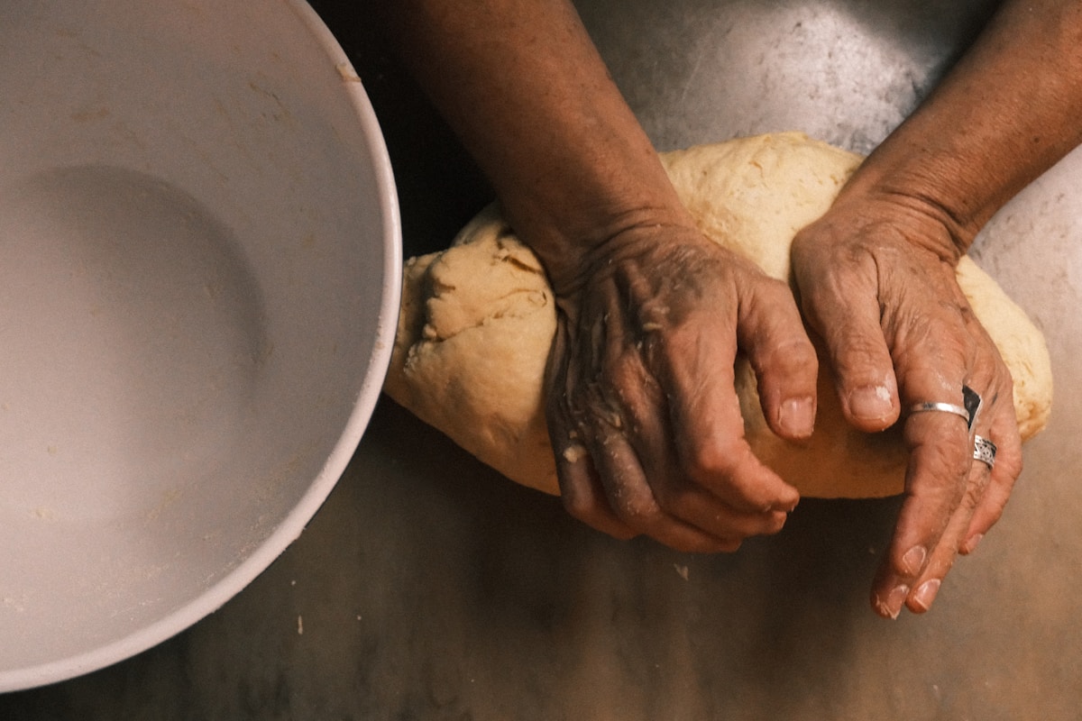 Hands kneading dough next to a white bowl