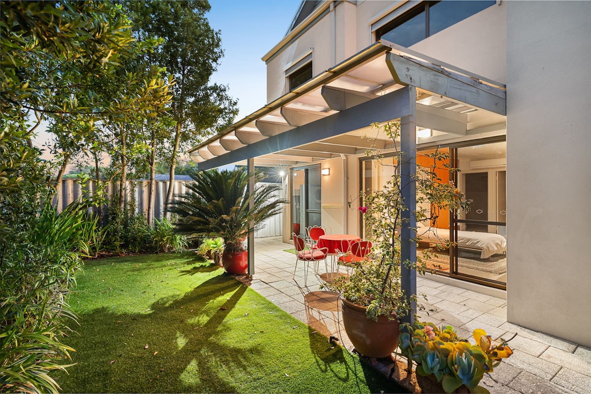Jardin luxuriant avec terrasse couverte et mobilier coloré.