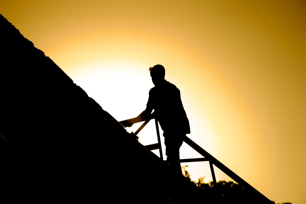 Silhouette d'une personne escaladant une montagne au coucher de soleil.