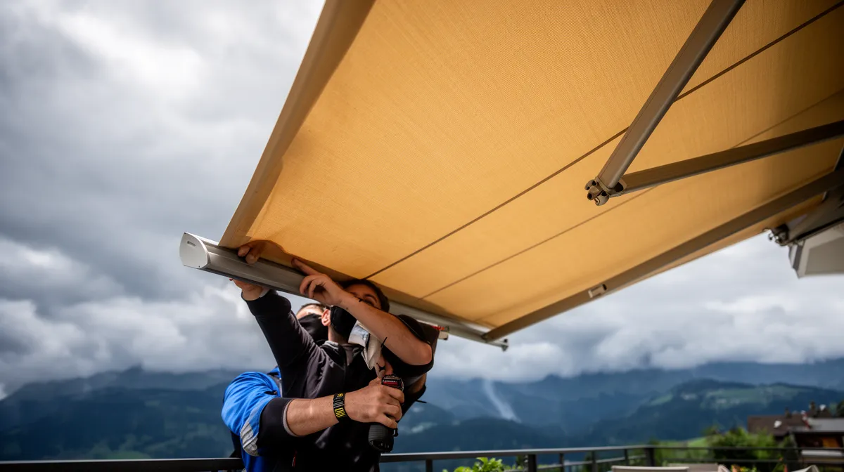 Personne installant une voile de soleil sur une terrasse avec vue sur les montagnes.