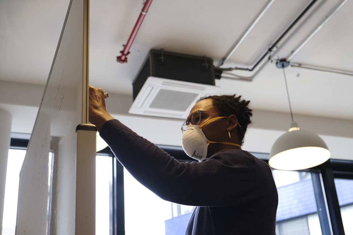 Homme en masque réparant un équipement électrique dans un bureau.