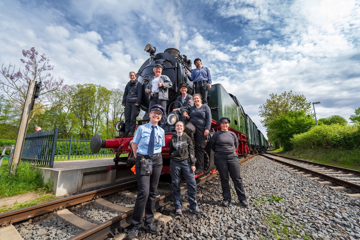 Groupe de personnes posant devant une locomotive à vapeur sur des voies ferrées.