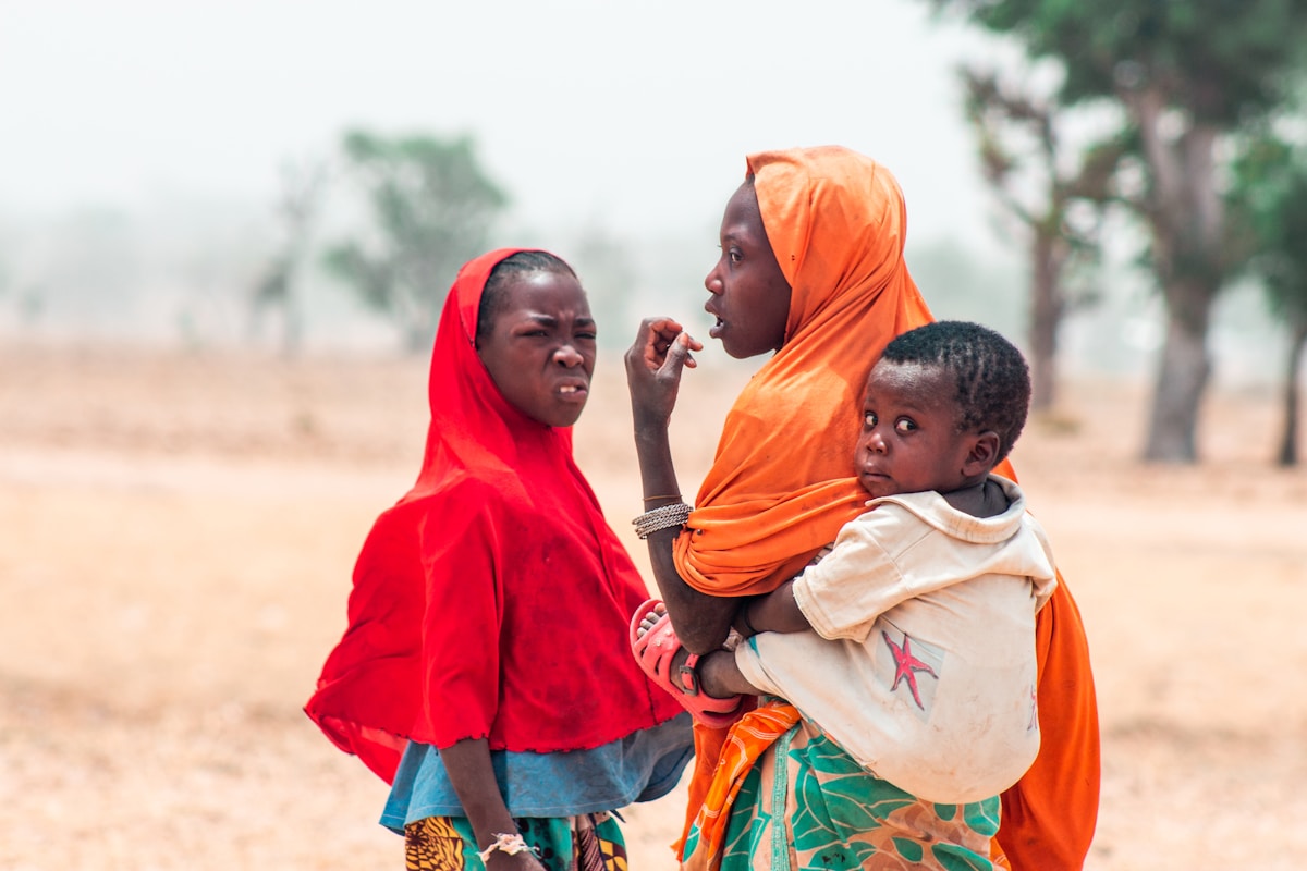 Deux femmes en vêtements colorés portant un enfant dans un environnement rural.