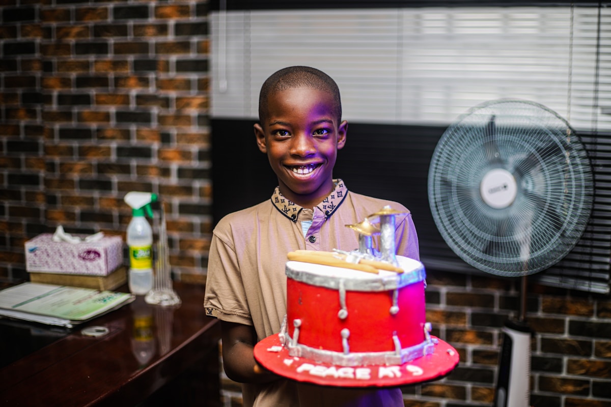 Jeune garçon souriant tenant un gâteau d'anniversaire rouge dans une pièce.