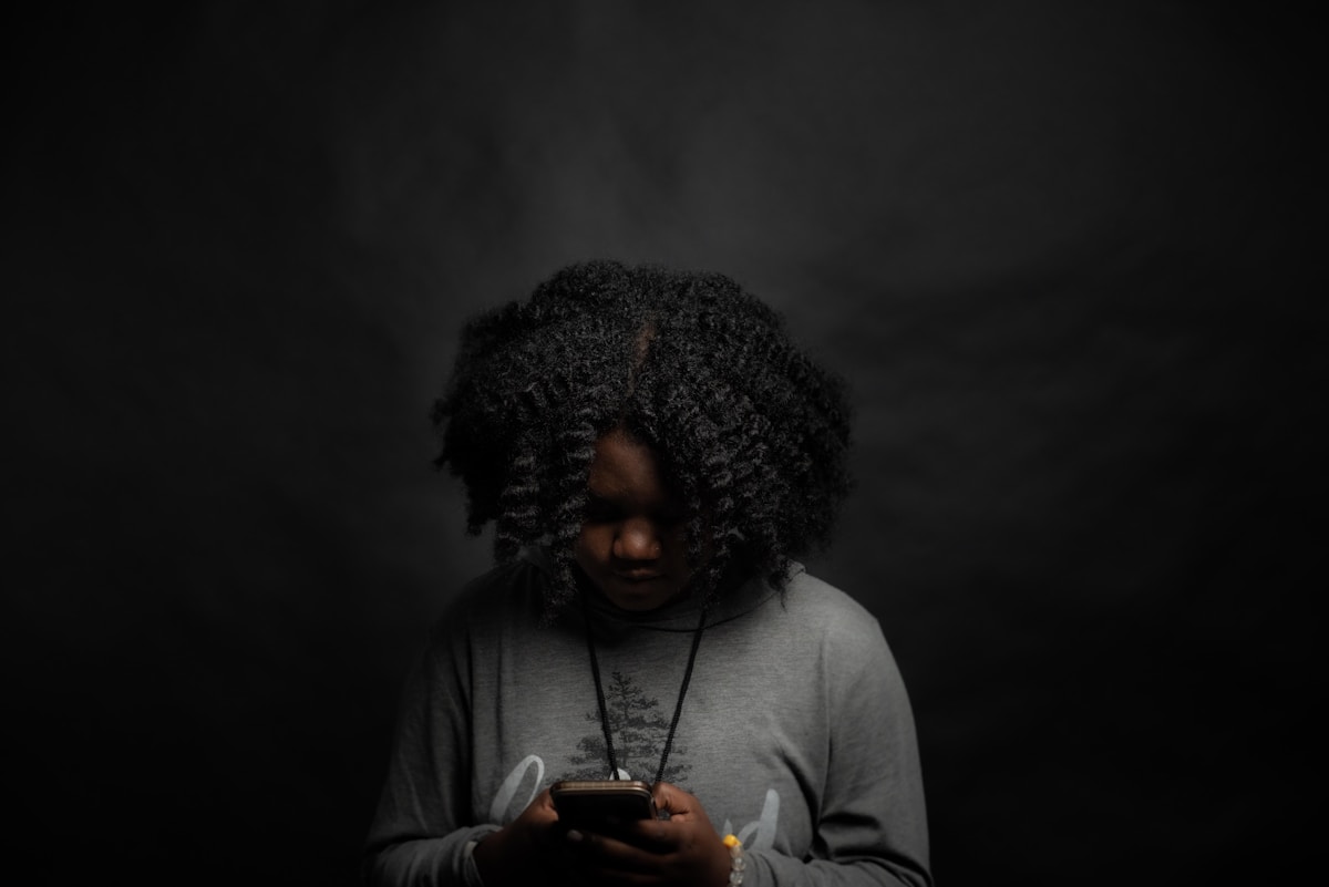 Jeune personne aux cheveux bouclés, utilisant un téléphone portable dans l'obscurité.