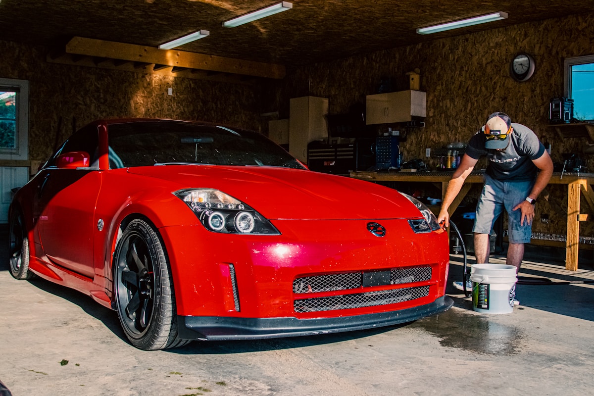 Voiture de sport rouge vif dans un garage, un homme en train de la nettoyer.