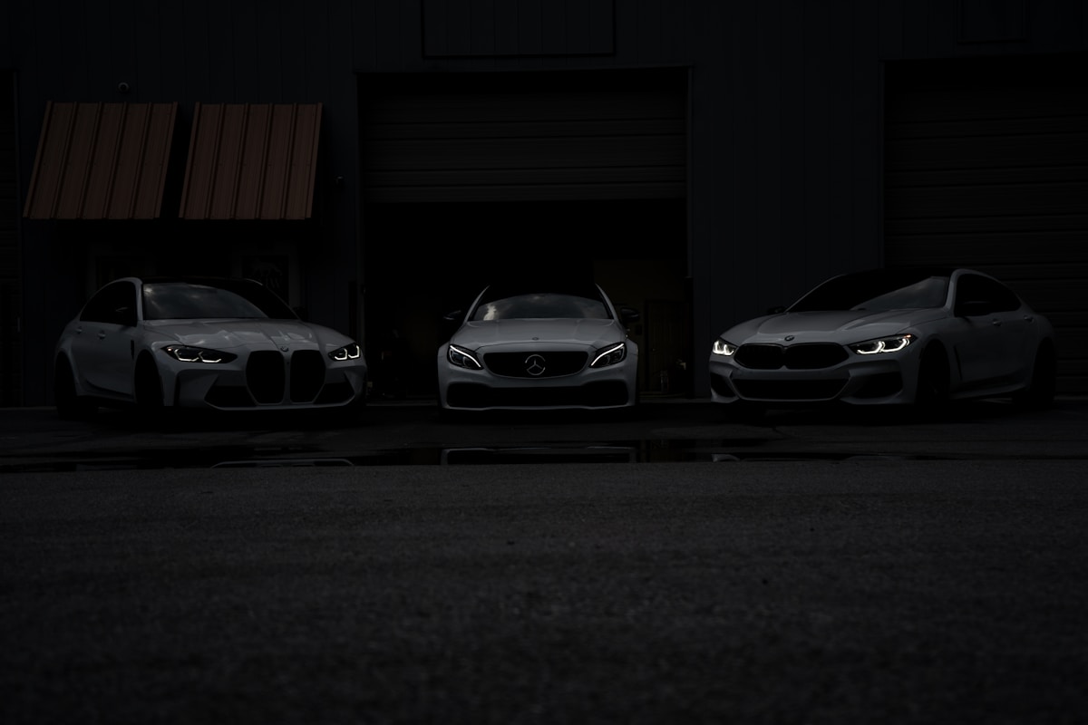 Trois voitures de luxe de marques différentes dans un garage sombre.