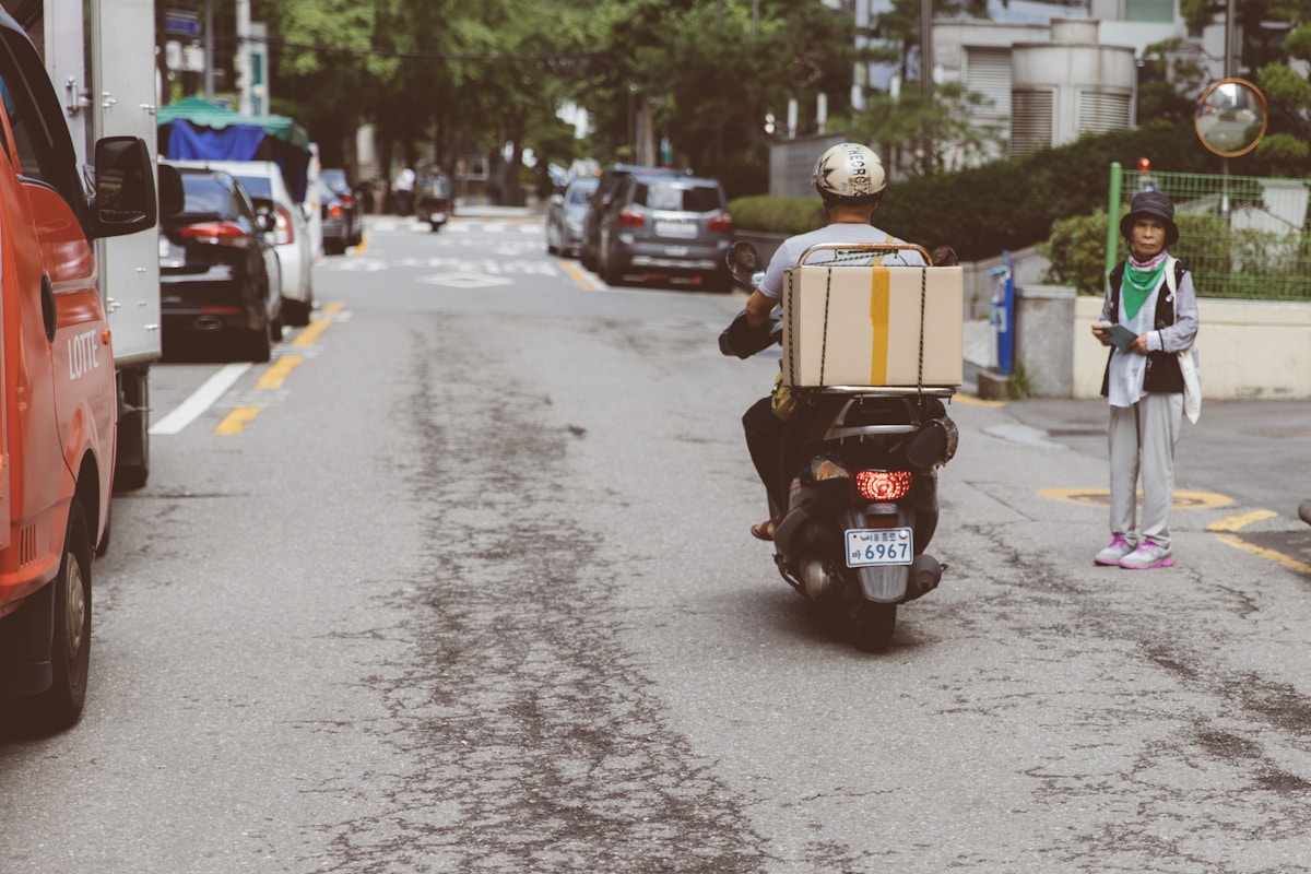 Livreur sur scooter transportant un colis dans une rue urbaine.