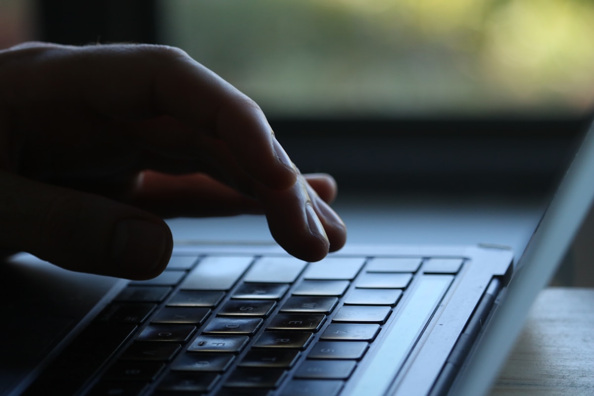 Main sur un clavier d'ordinateur portable dans un environnement sombre.