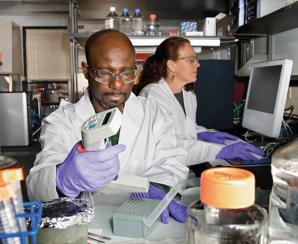 Deux scientifiques dans un laboratoire, l'un utilisant un appareil de mesure, l'autre travaillant sur un ordinateur.