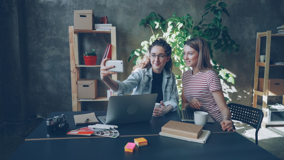 Deux femmes prennent un selfie sur un bureau.